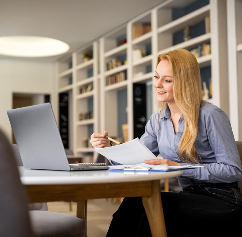 Business Woman Reviewing Paperwork And Smiling While Looking At Laptop